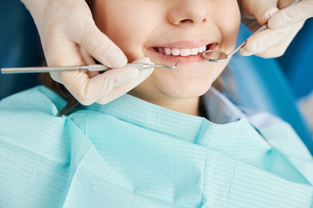Pediatric dentist examining child's teeth during visit for sensitive teeth treatment and tooth extraction at Kids Smiles Pediatric Dentistry in St. Louis.
