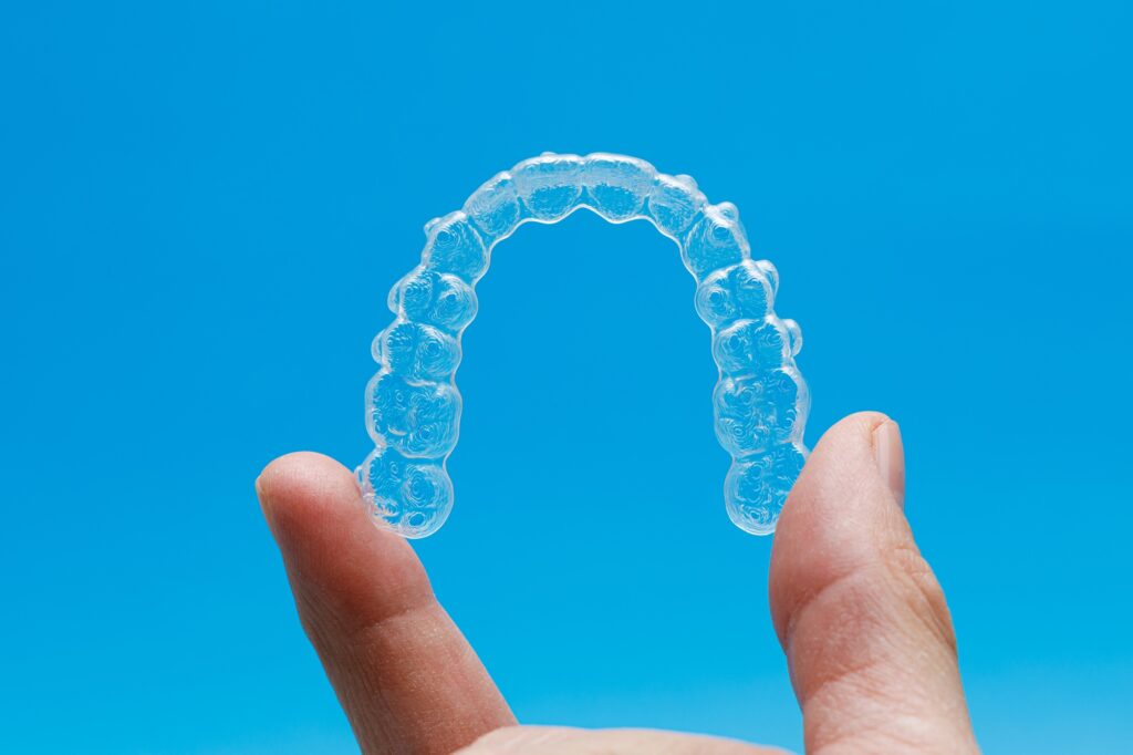 Close-up of clear aligners held against a blue background, representing CandidPro orthodontic treatment at Kids Smiles Pediatric Dentistry in St. Louis